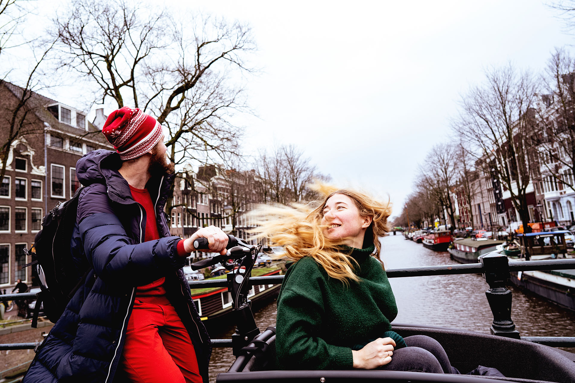 man rijdt bakfiets met vrouw voorin aan een gracht