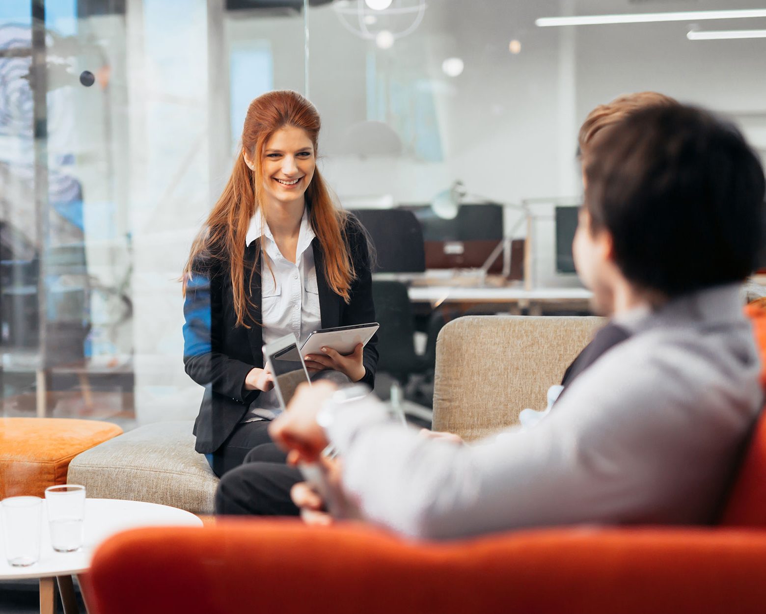 vrouw met tablet praat tegen man op bank, kantoor